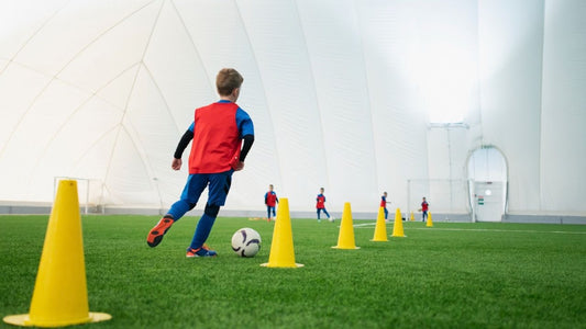 Kid practicing zig-zag dribbling around soccer training cones.